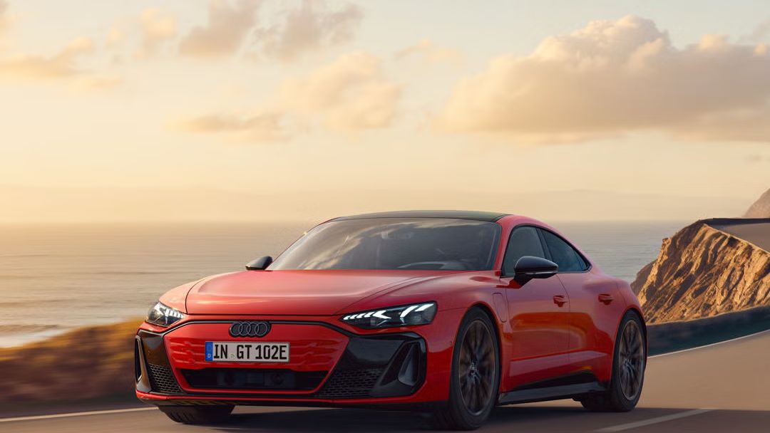 Der e-tron GT quattro fährt auf einer kurvigen Küstenstraße bei Sonnenschein, zur Linken das Meer, zur Rechten felsiges Gebirge.