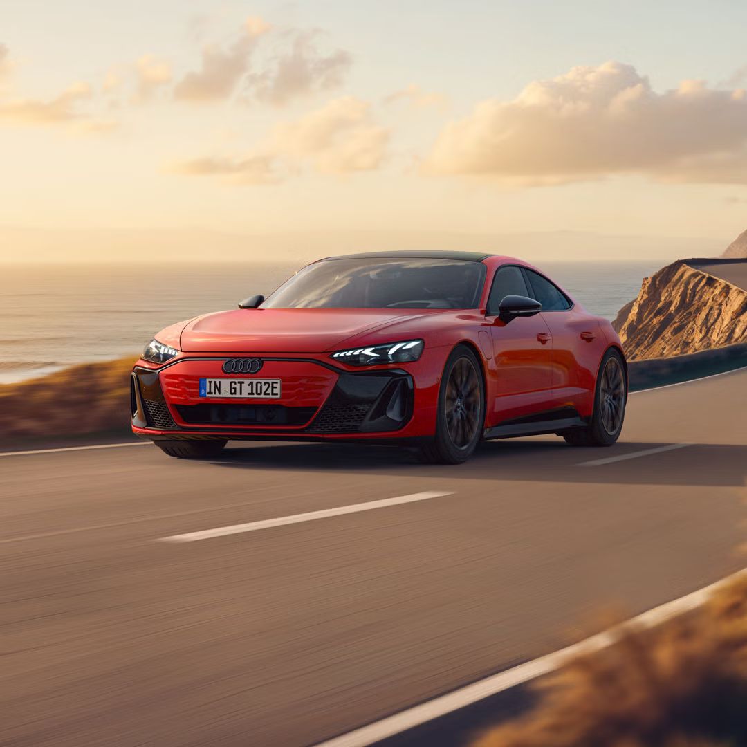 Der e-tron GT quattro fährt auf einer kurvigen Küstenstraße bei Sonnenschein, zur Linken das Meer, zur Rechten felsiges Gebirge.