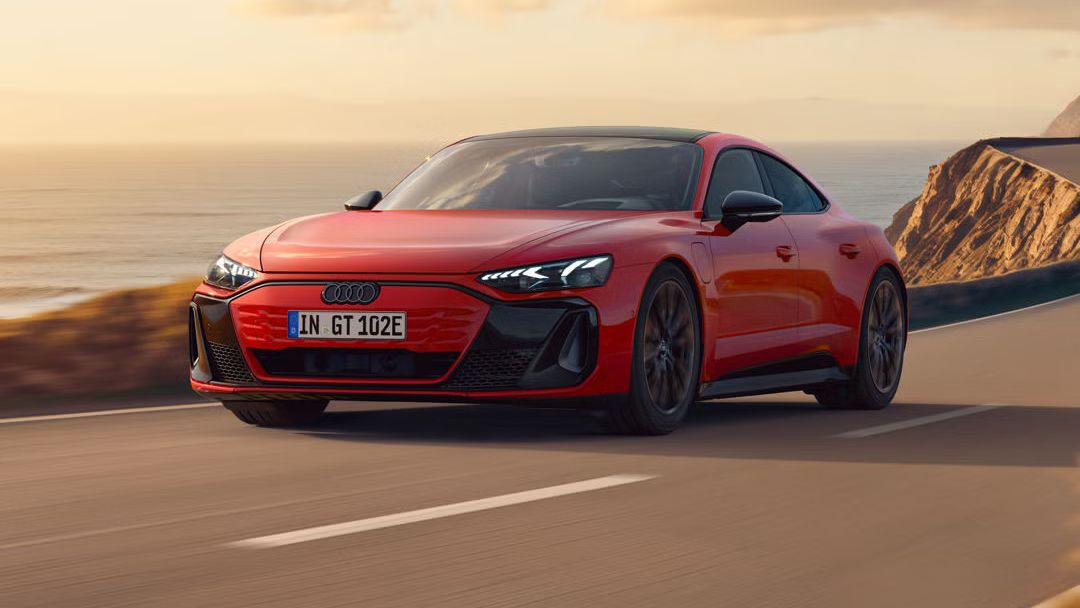 Der e-tron GT quattro fährt auf einer kurvigen Küstenstraße bei Sonnenschein, zur Linken das Meer, zur Rechten felsiges Gebirge.