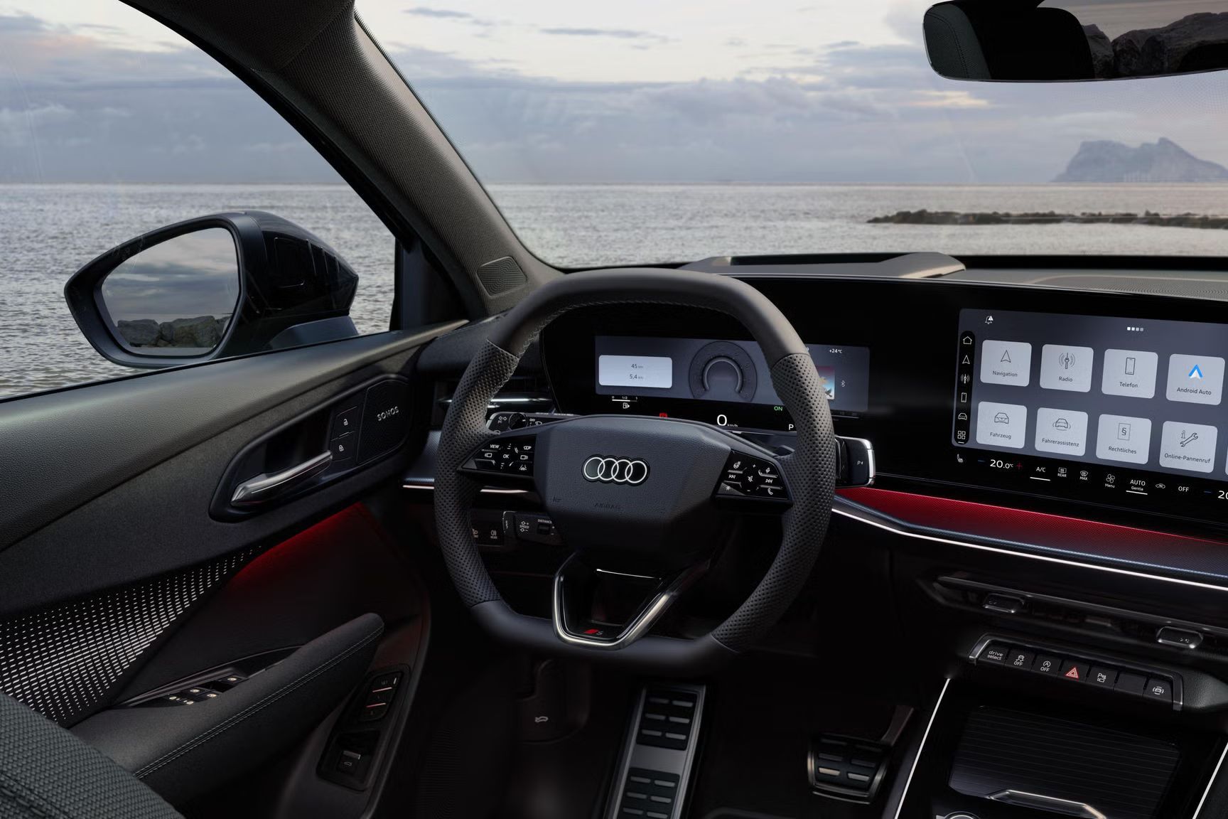 Blick von hinten auf das Cockpit des Q3 SUV mit Lenkrad, Panoramadisplay und rotem Ambiente-Lichtpaket. Durch die Frontscheibe ist das Meer zu sehen.