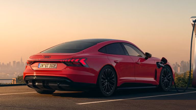 Ein roter Audi e-tron GT quattro steht auf einer Anhöhe über einer Stadt und wird an einer öffentlicher Ladesäule geladen.