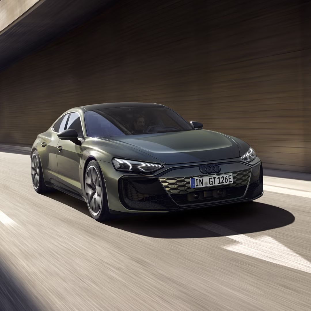 Grüner Audi RS e-tron GT performance fährt unter einer Betonbrücke auf einer mehrspurigen Straße mit Bewegungseffekt.
